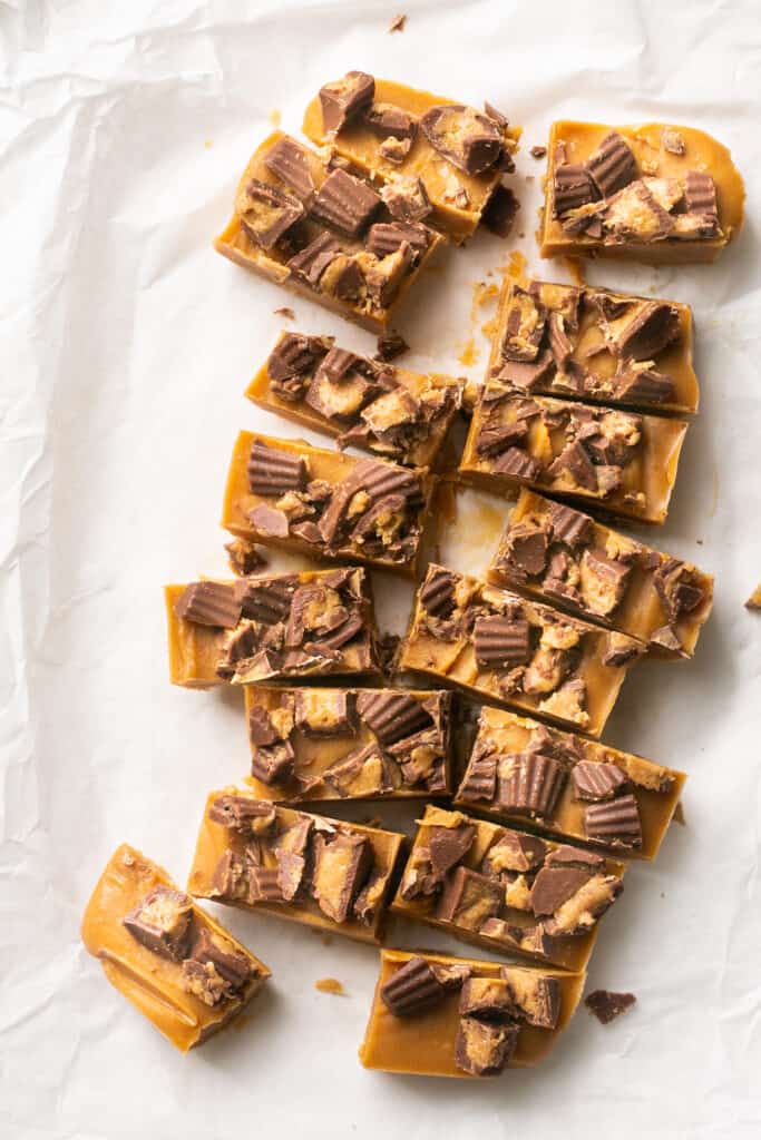 4 ingredient peanut butter fudge topped with peanut butter cups cut into bars on parchment paper