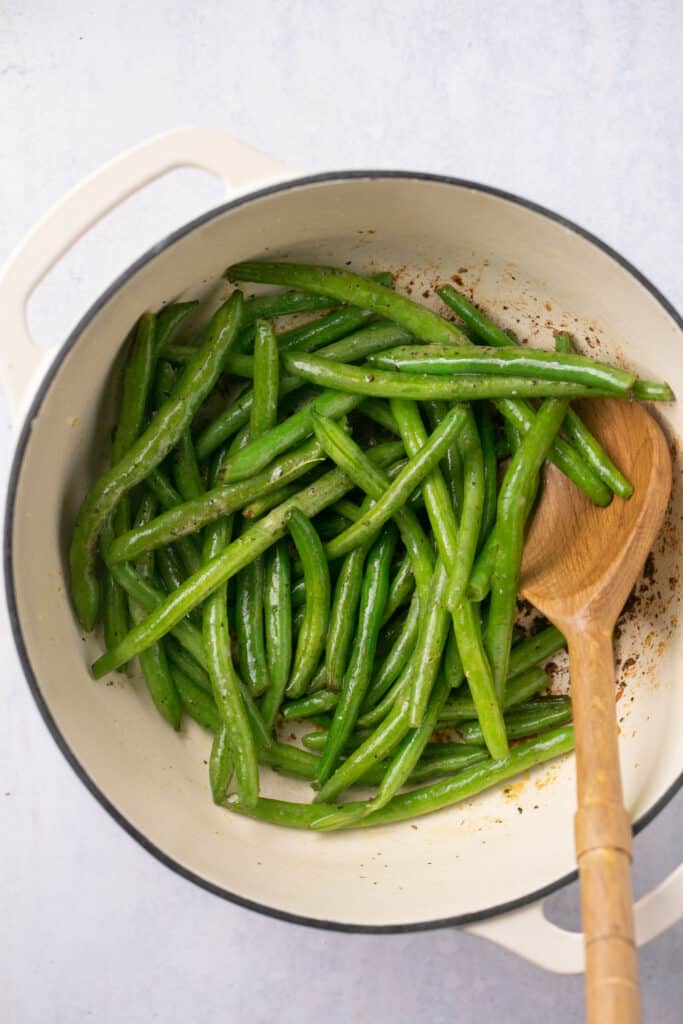 Green beans in a dutch oven with a wooden spoon.