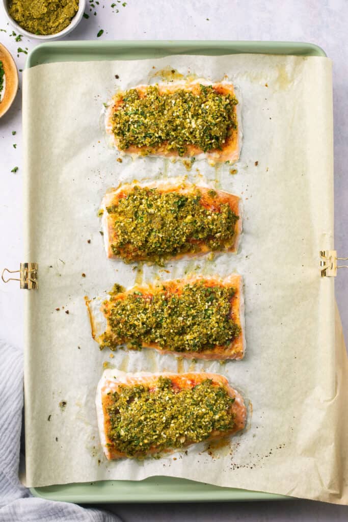 Baked pesto salmon on a baking sheet with parchment paper
