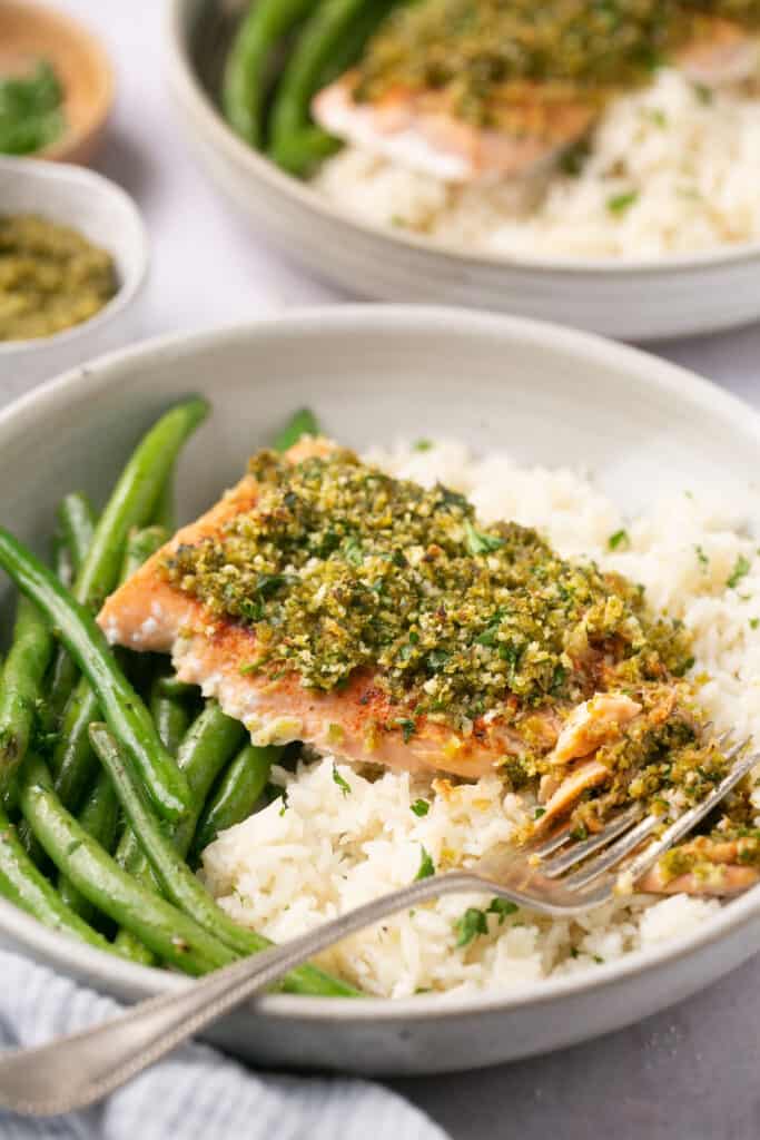 Pesto salmon with rice and green beans in a bowl with a fork