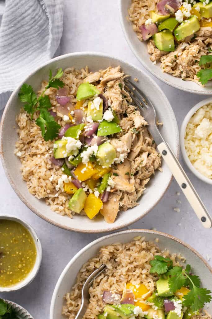 Salsa verde chicken topped with peppers and onions served in bowls with forks.