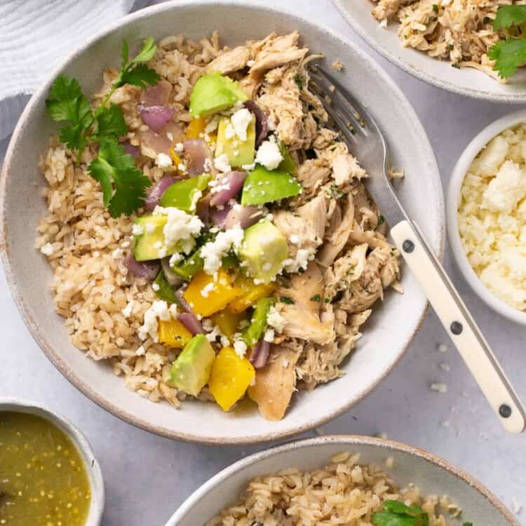 Salsa verde chicken topped with peppers and onions served in bowls with forks.