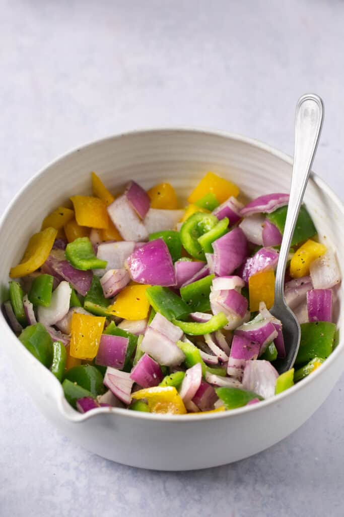 Peppers and onions in a bowl with a spoon.