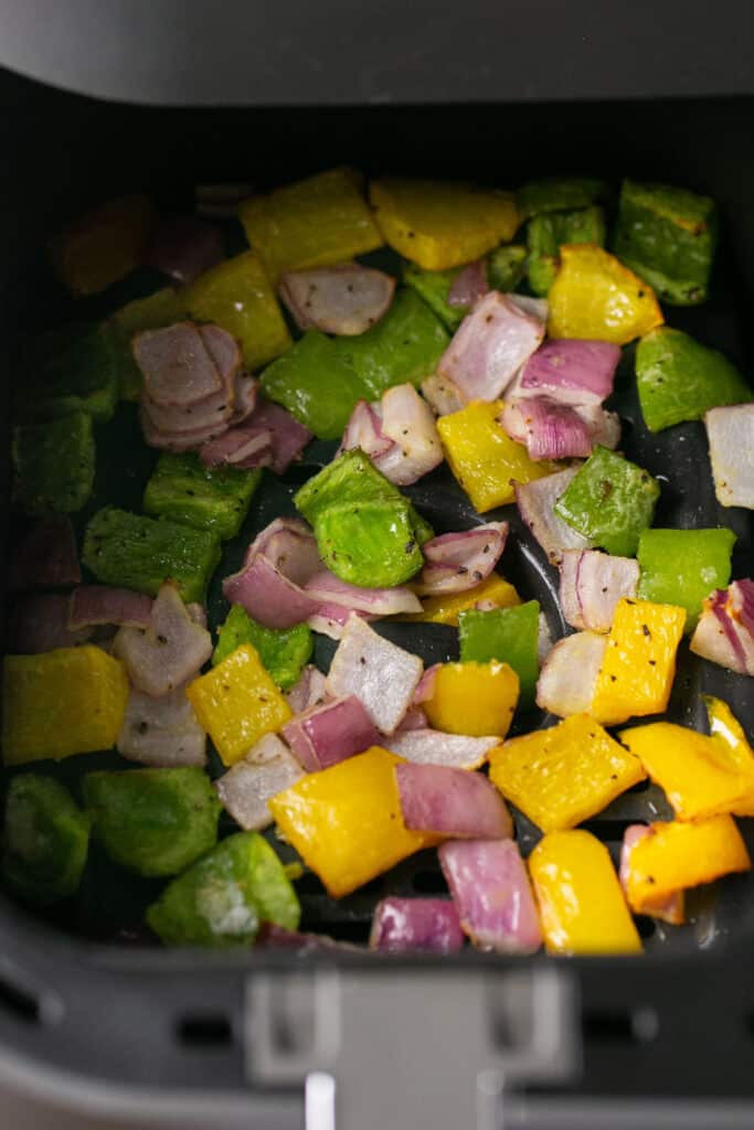 Peppers and onion in an air fryer basket.