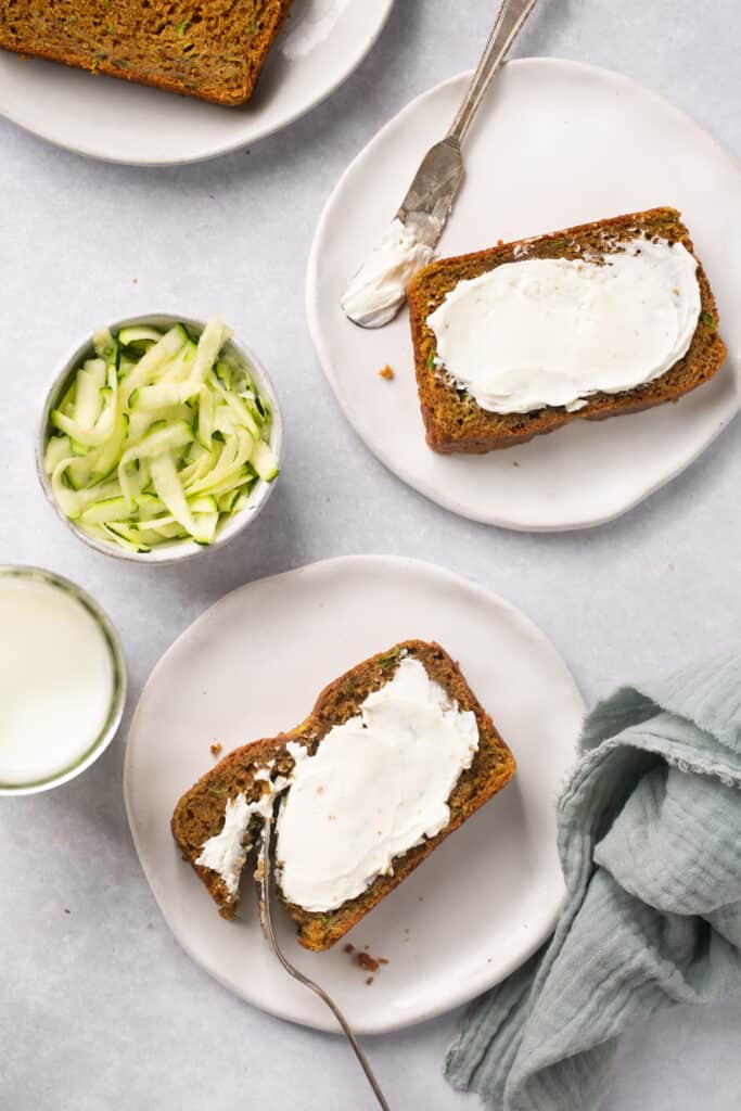 Sliced healthy gingerbread zucchini bread topped with cream cheese on small plates with forks.