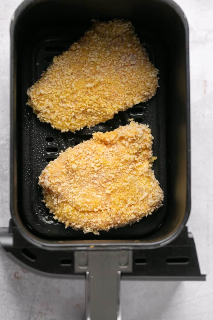 Two chicken patties in an air fryer basket before being cooked.