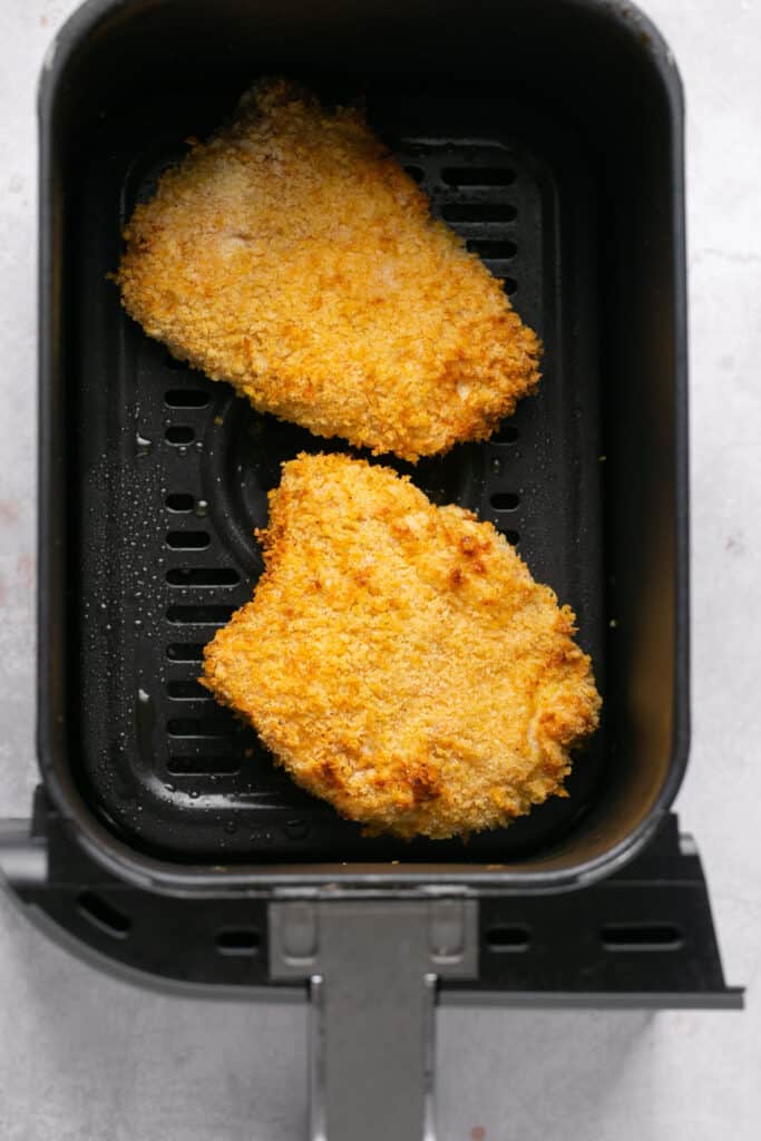 Two chicken patties in an air fryer basket after being cooked.