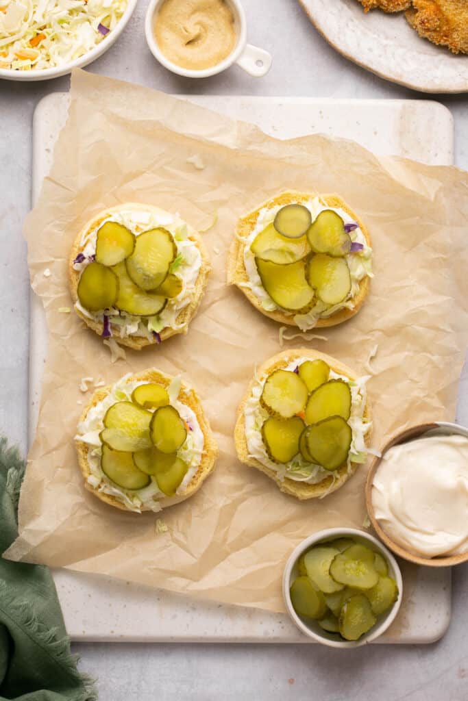 Four bottom buns topped with pickles and mayo on parchment paper.