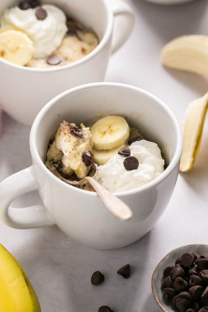 Banana mug cake in a mug topped with chocolate chips, bananas, and whipped cream.