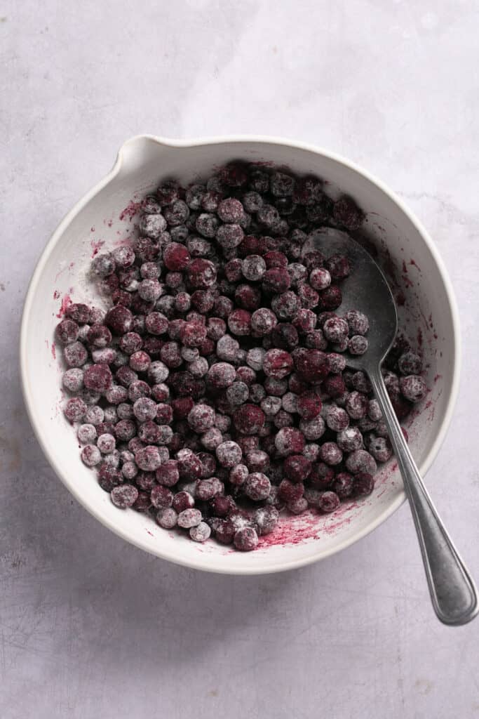 Blueberries and flour in a mixing bowl with a spoon.