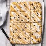 Bo-berry bars topped with icing and cut into squares on a cooling rack with parchment paper.