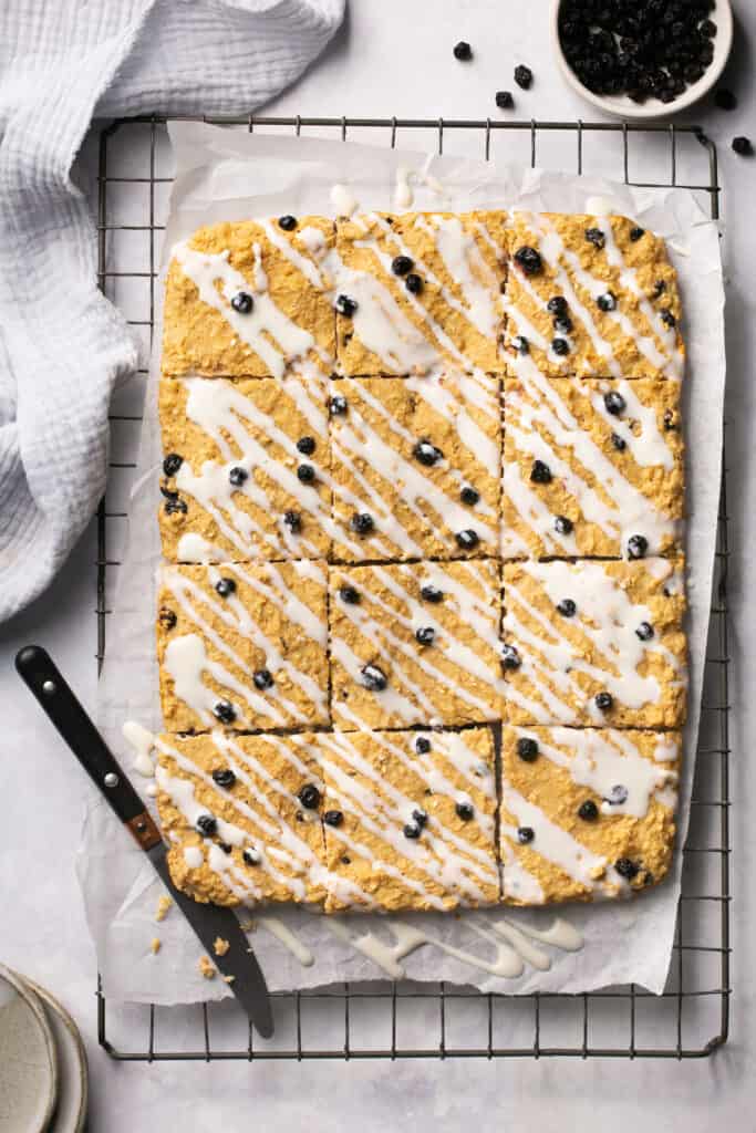 Bo-berry bars topped with icing and cut into squares on a cooling rack with parchment paper.