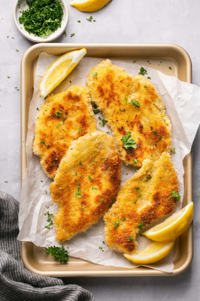 Crispy chicken schnitzel on a tray with parchment paper garnished with lemon slices