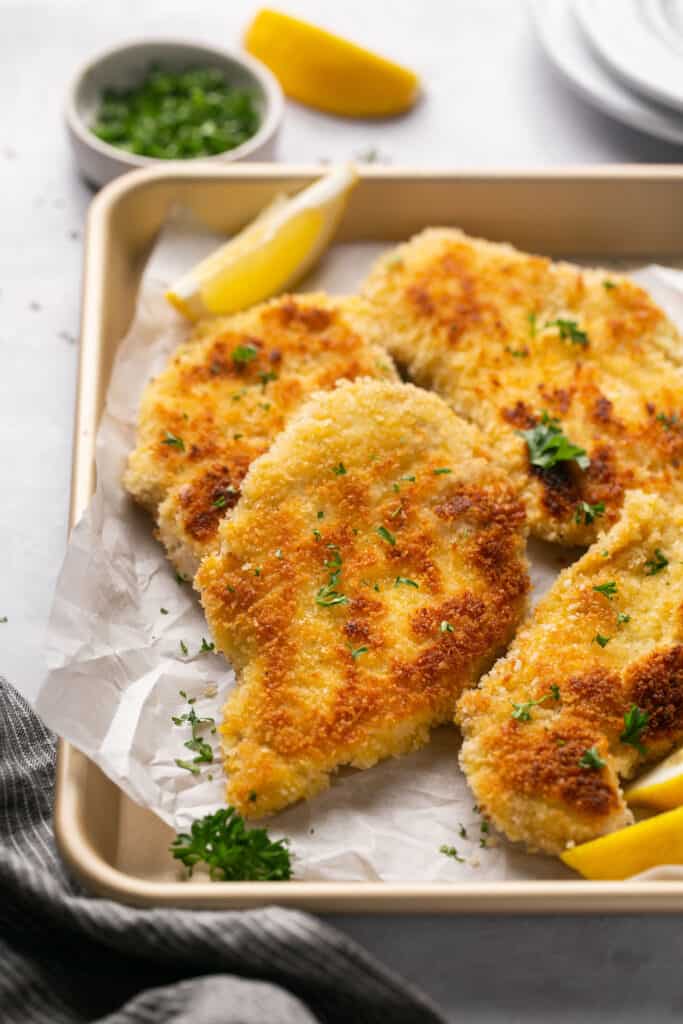 Healthy chicken schnitzel in a baking pan with parchment paper.