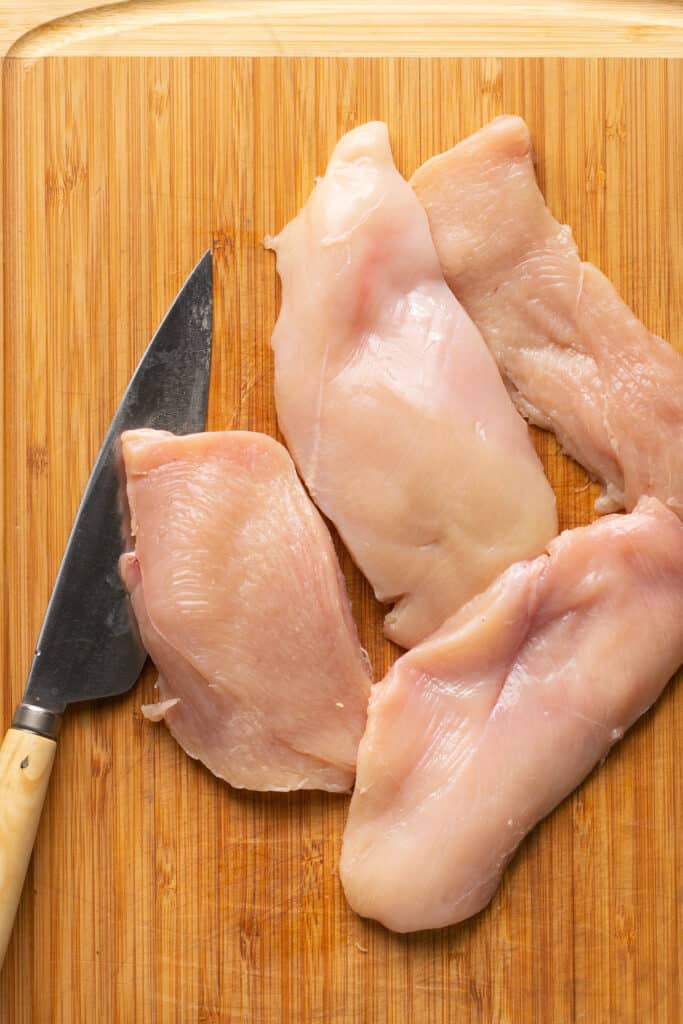 Raw chicken breasts on a cutting board with a knife.