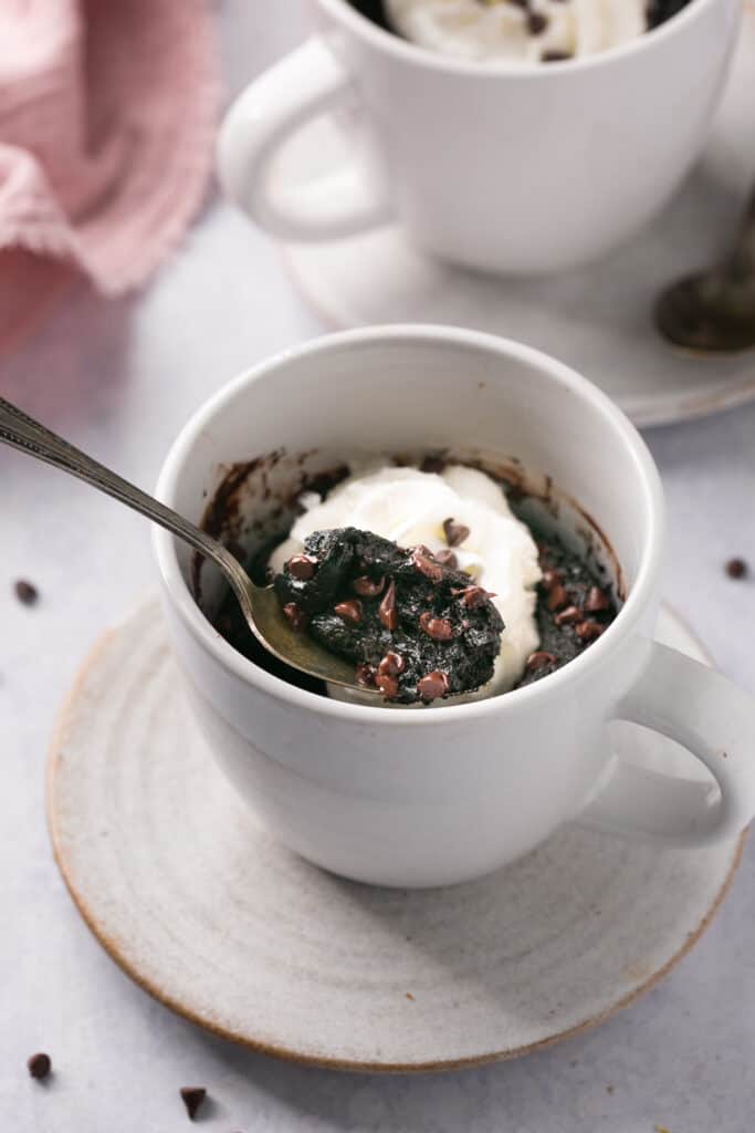 Chocolate protein lava cake topped with whipped cream in a mug with a spoon.