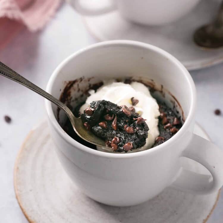 Chocolate protein lava cake topped with whipped cream in a mug with a spoon.
