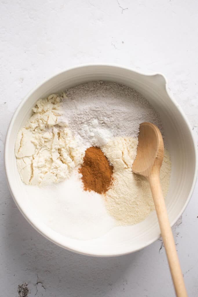 Dry ingredients for cinnamon sugar protein cake bars in a glass bowl with a wooden spoon.