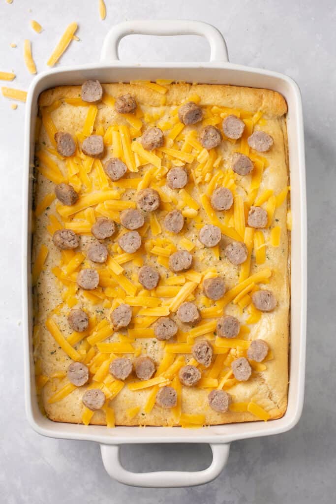 Sliced sauage and cheese on top fo the eggs and crescent dough in a baking dish.