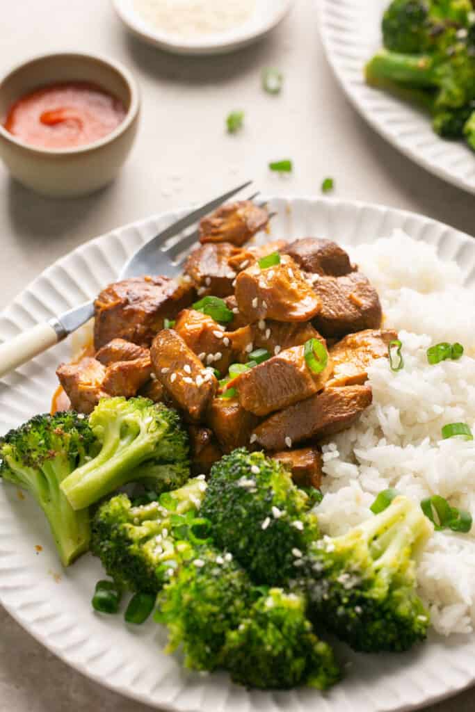Zoomed in view of honey sriracha chicken with rice and broccoli on a plate with a fork.