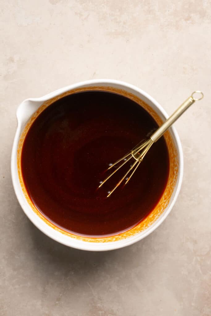 Sauce for honey sriracha chicken in a small bowl with a whisk