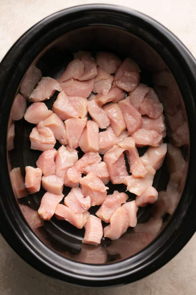 Pieces of raw chicken in a slow cooker.