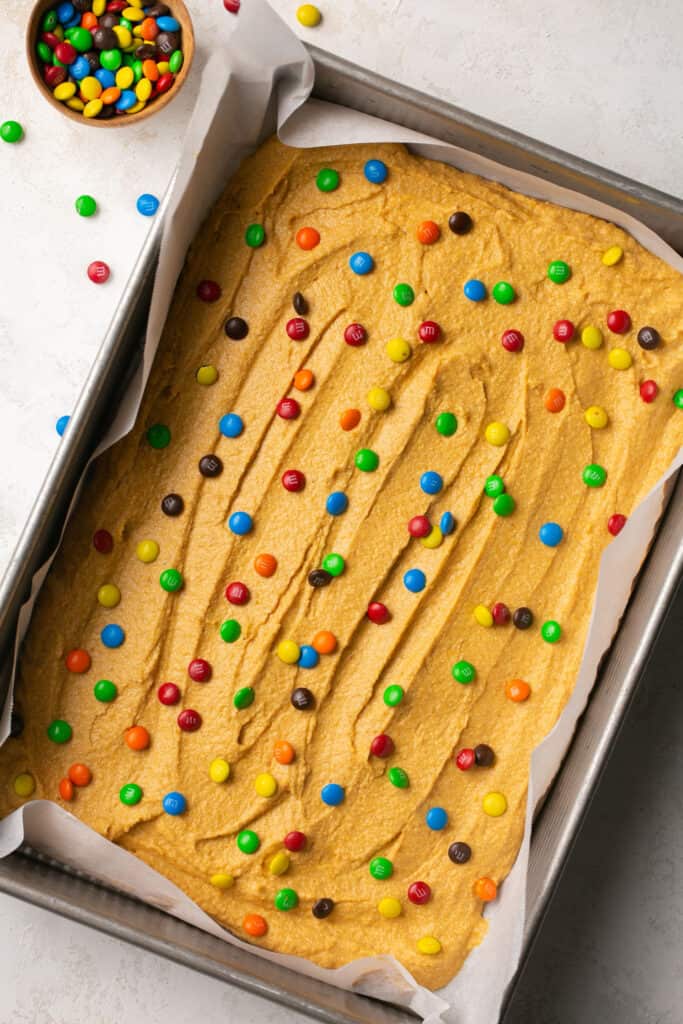 Soft Baked M&M Pumpkin Protein Oat Bars in a baking pan with parchment paper before being baked.