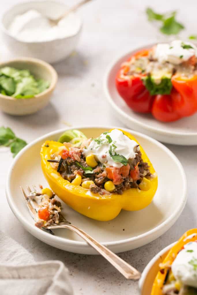 Healthy stuffed peppers with ground beef topped with sour cream on a small plate with a fork