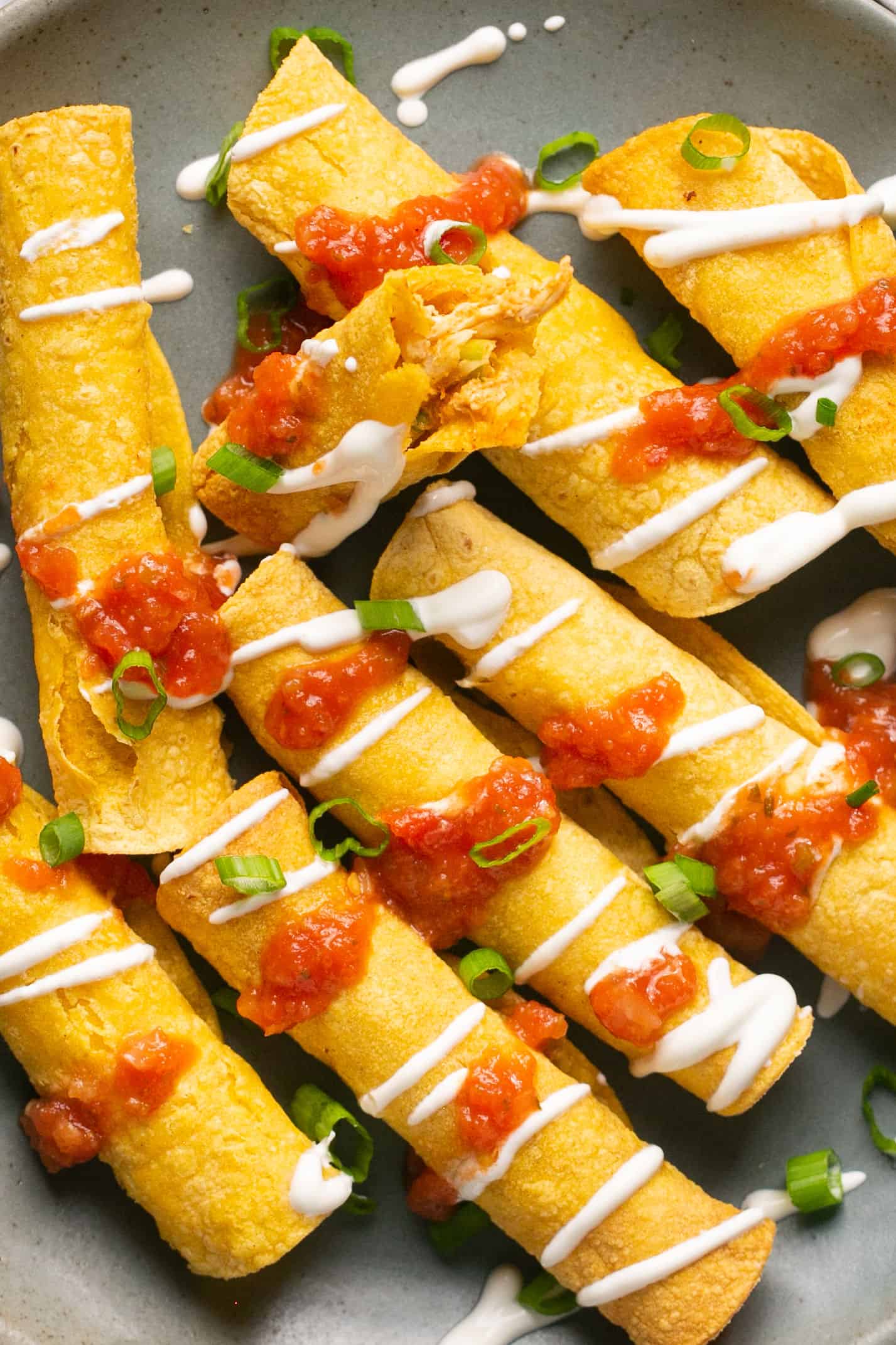 Air fryer chicken taquitos topped with salsa and sour cream on a plate.