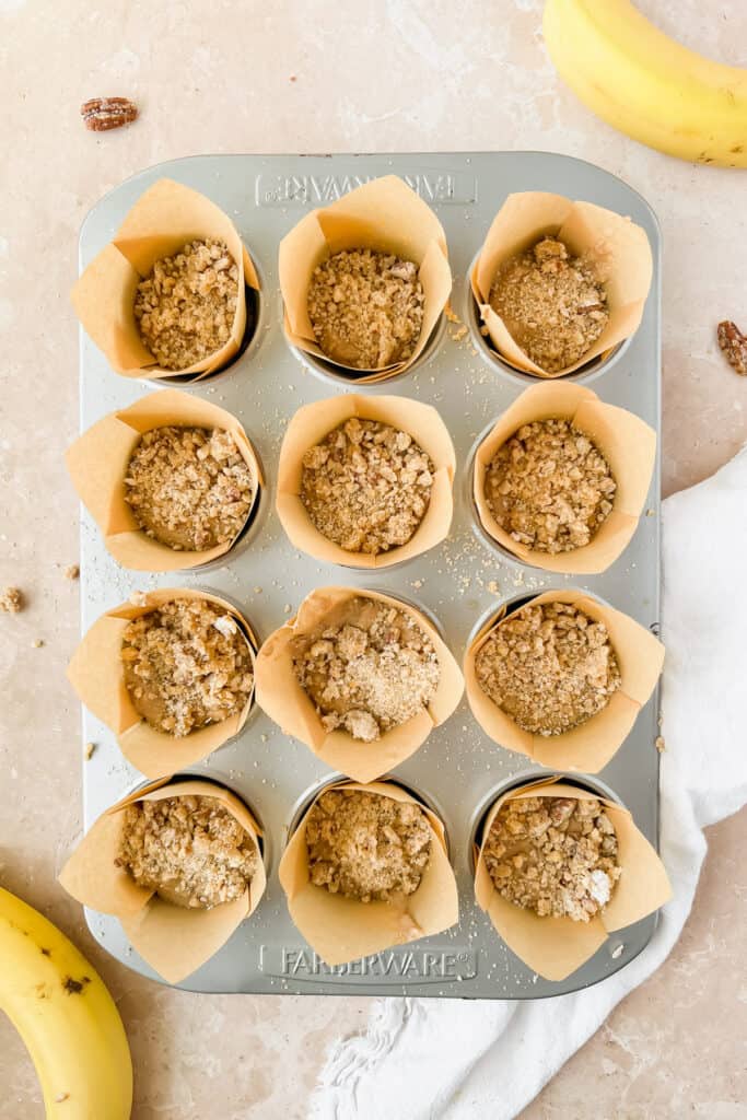Banana nut protein muffins topped with pecan crumble in a muffin pan before being baked.