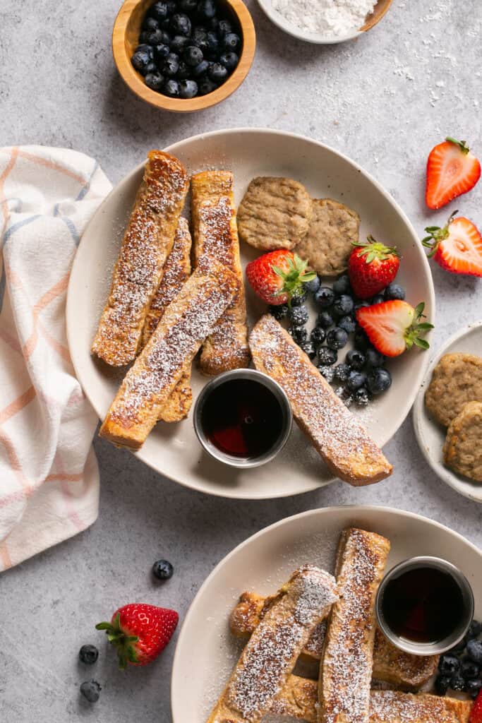Protein french toast sticks on a plate with fruit and side of syrup.