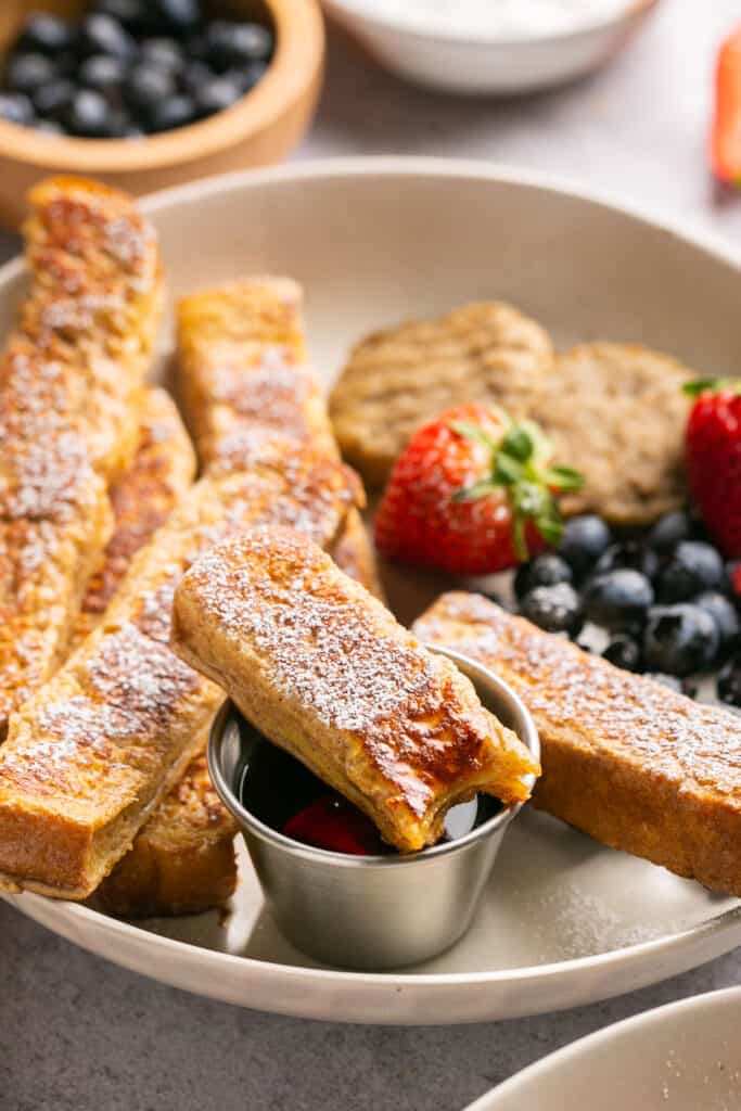 Protein french toast sticks on a plate with fruit and side of syrup