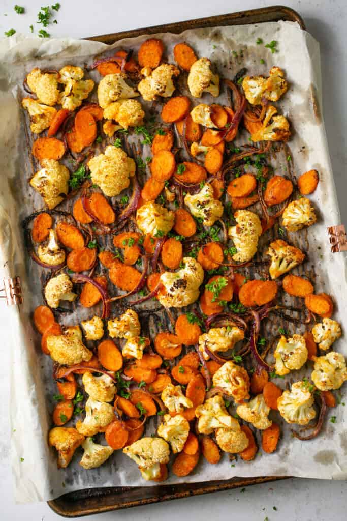 Roasted cauliflower and carrots on a baking sheet with parchment paper