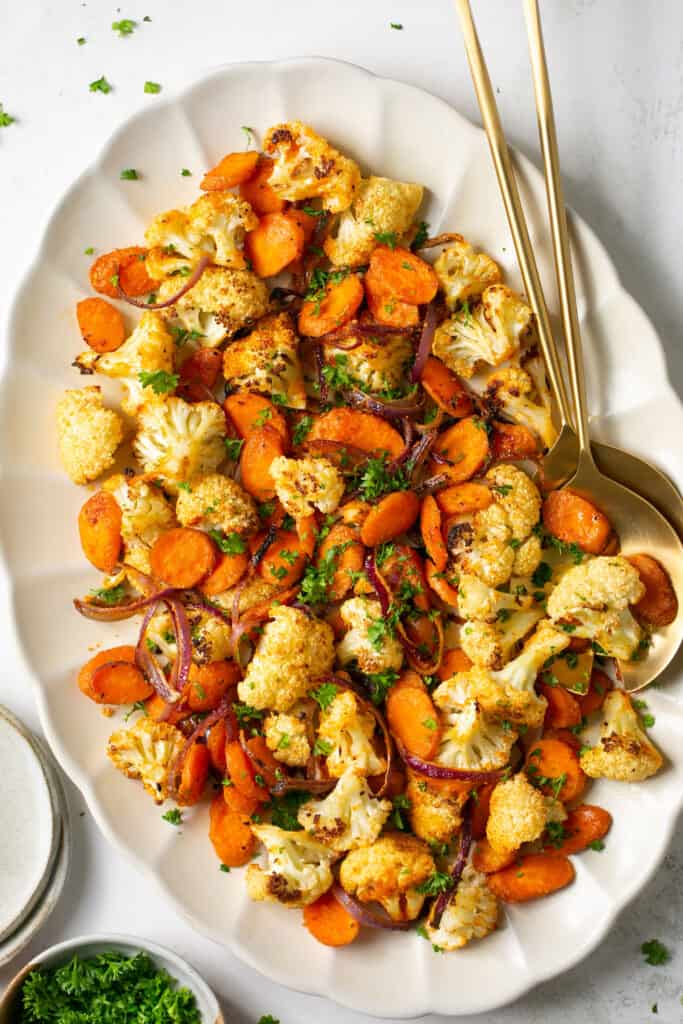 Roasted cauliflower and carrots in a serving dish with serving spoons