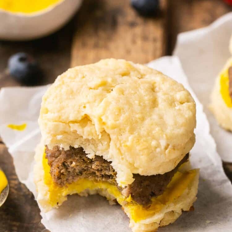 A healthy sausage biscuit with a bite taken out of it on a square of parchment paper.