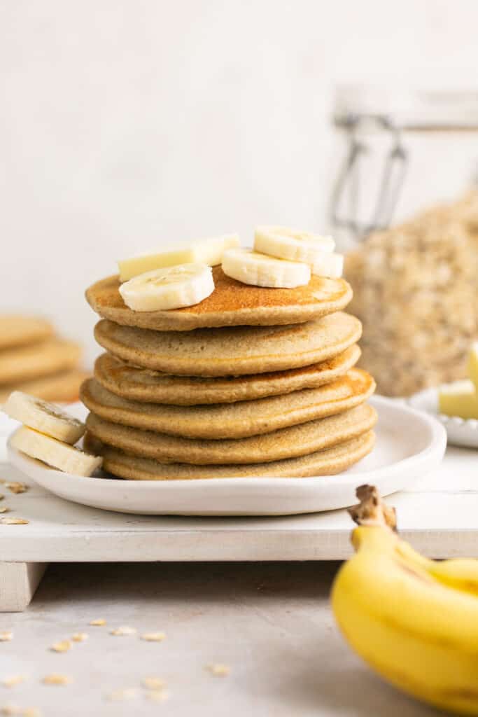 Blender banana oatmeal pancakes in a stack on a plate topped with banana slices.