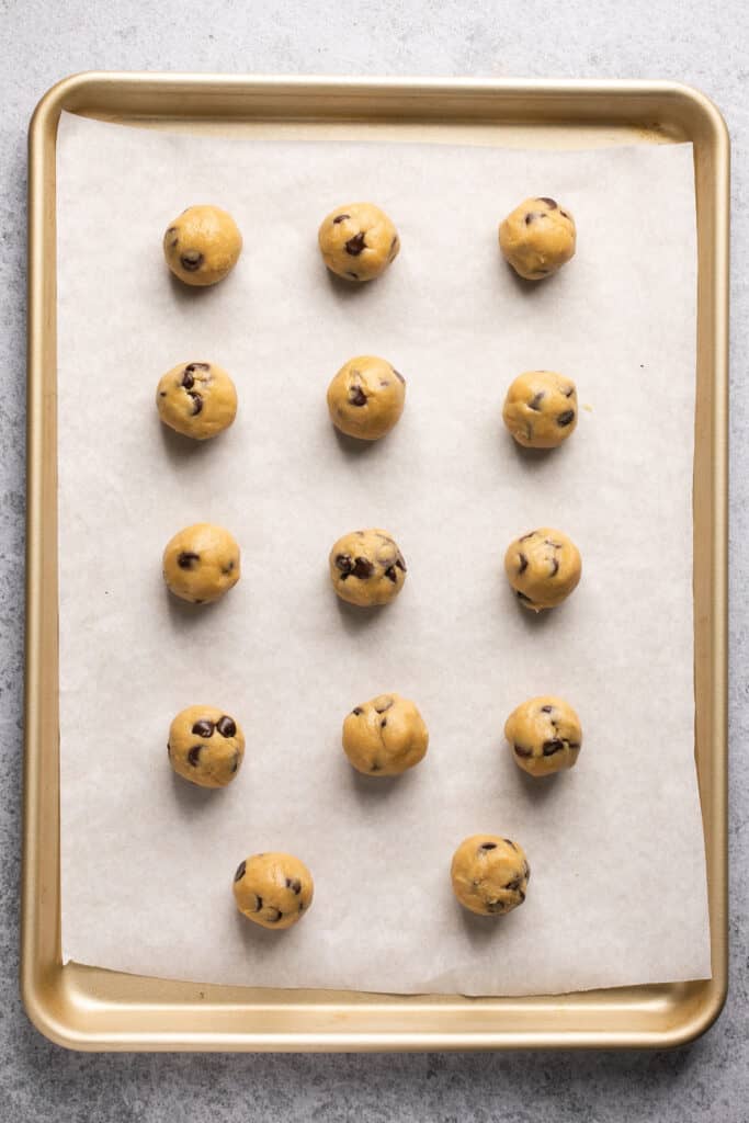 Rolled balls of cookie dough on a baking sheet with parchment paper.