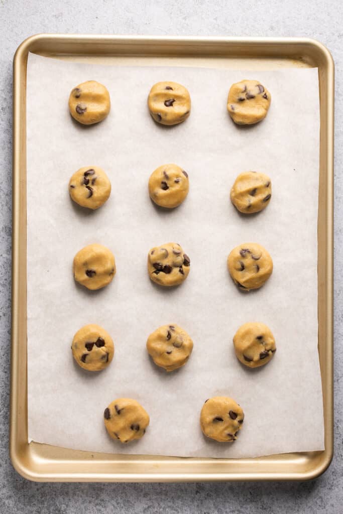 Balls of cookie dough flattened on a baking sheet with parchment paper.