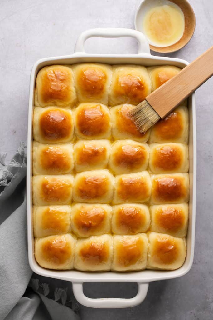 Honey butter yeast rolls in a baking dish being brished with honey butter after being baked.