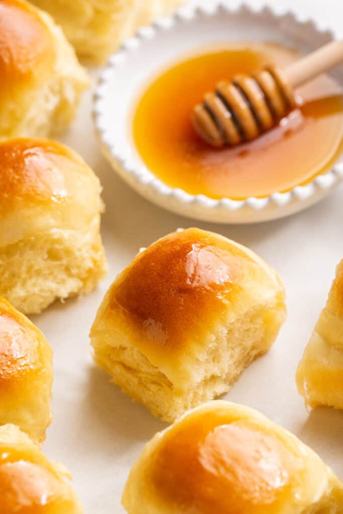 Honey butter yeast rolls on parchment paper with a side of honey.