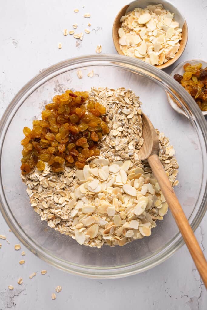 Dry ingredients for honey almond granola in a mixing bowl with a wooden spoon before being mixed together