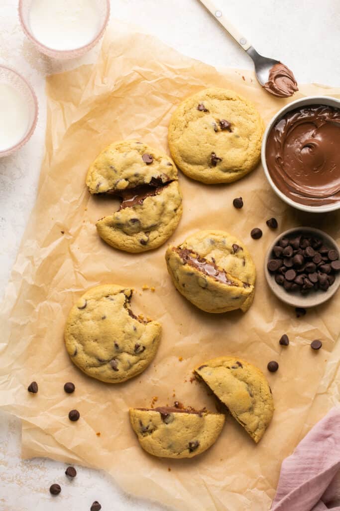 Nutella stuffed chocolate chip cookies, some broken in half on parchment paper.