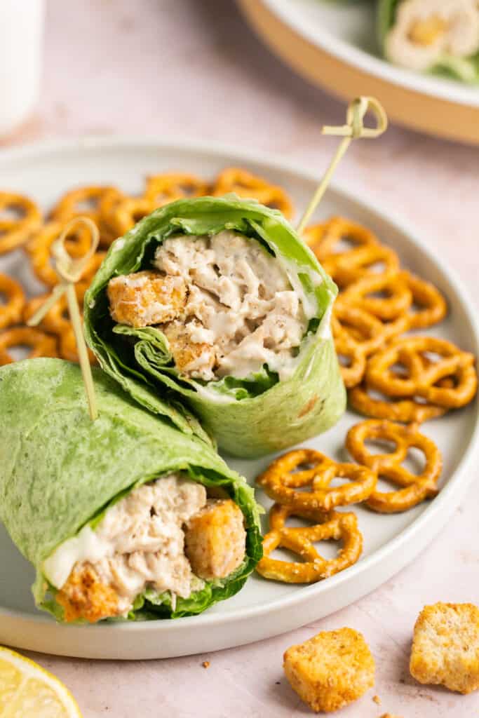 Chicken Caesar Wrap cut in half served on a plate with a side of pretzels