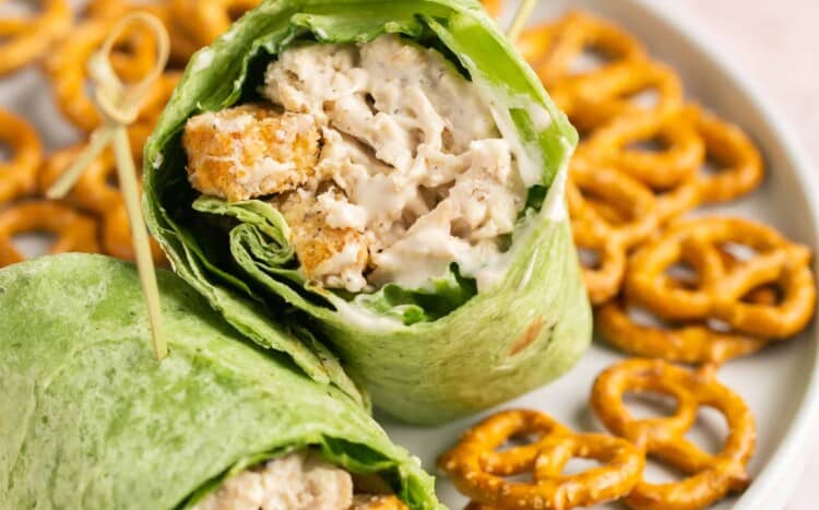 Healthy chicken caesar wrap cut in half on a plate with a side of pretzels.