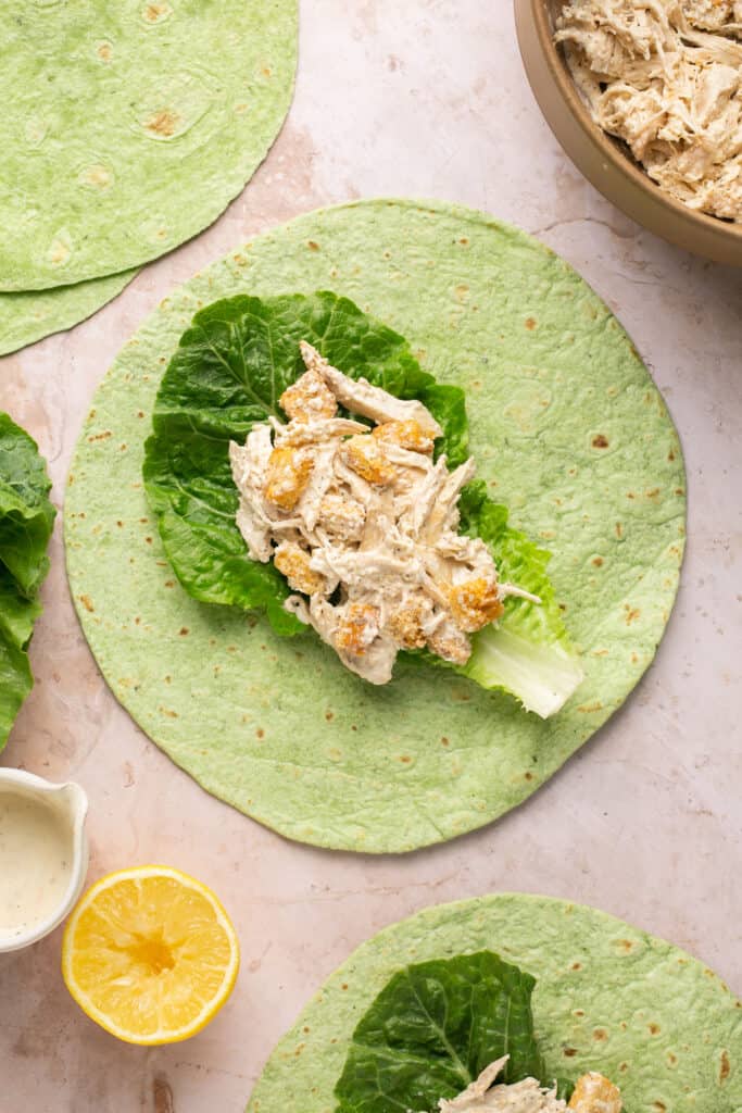 Spinach tortilla wrap with romain lettuce leaf and chicken mixture on top.