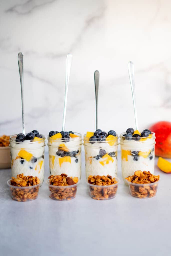 Greek yogurt parfaits with fruit in mason jars with spoons and granola served on the side