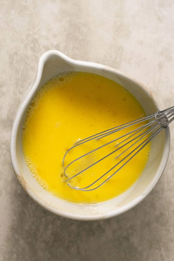 Eggs and egg whites whisked together in a mixing bowl with a whisk.