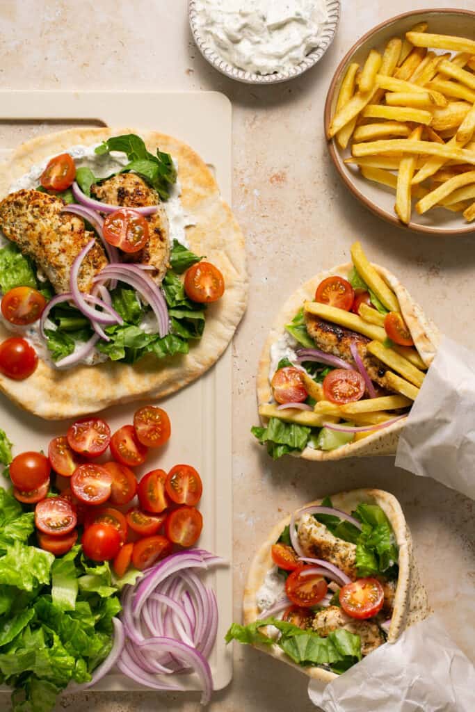 Healthy chicken gyros on a cutting board and wrapped up with a side of fries and tzatziki sauce.