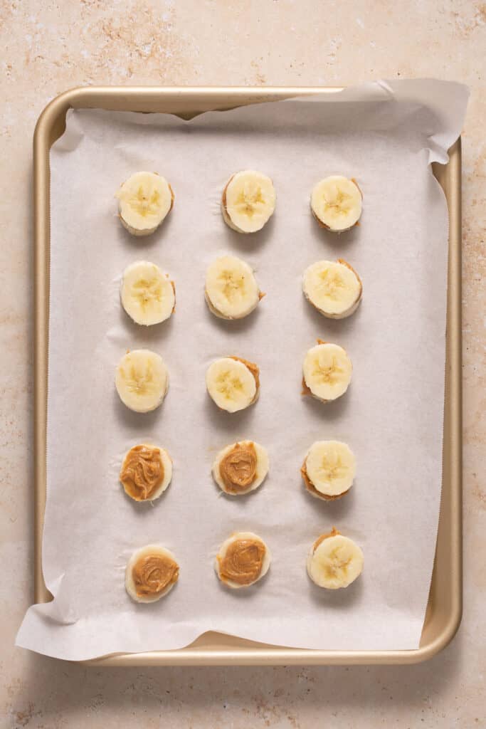 Banana slices being spread with peanut butter and topped with another banana slice.