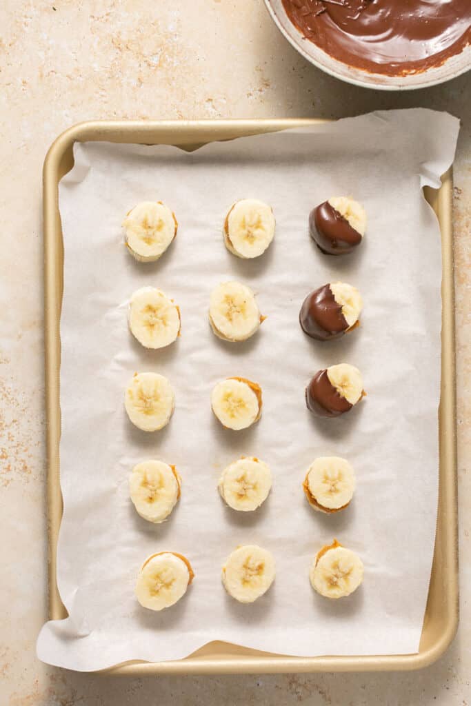 Banana slices with peanut butter in sandwiched in the middle being dipped in melted chocolate.